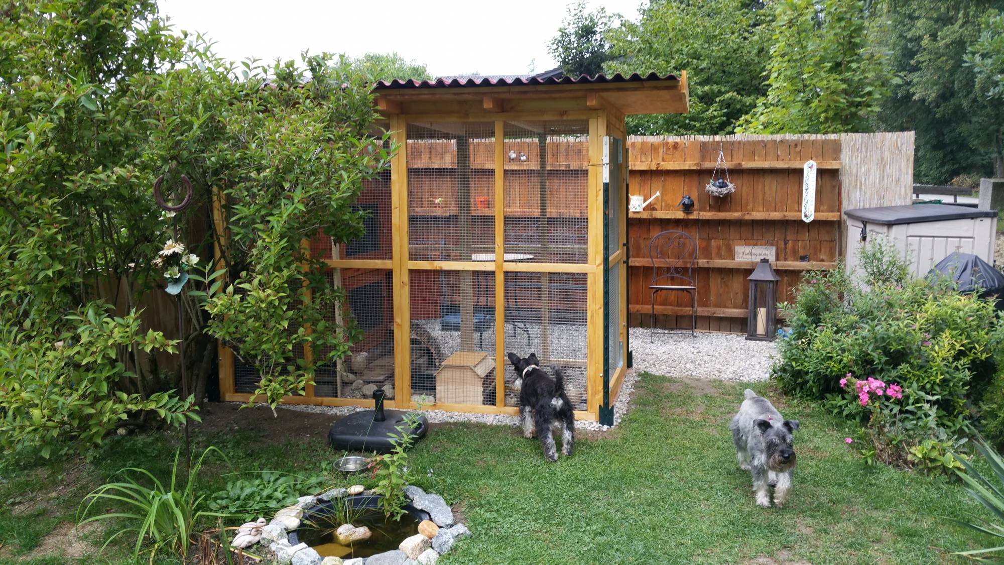 In einem Garten einer Kundin steht die Sonderanfertigung einer Voliere mit Dach.